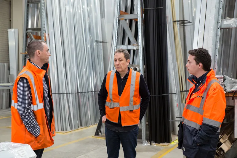 Team in high-visibility vests conversing in a metal warehouse