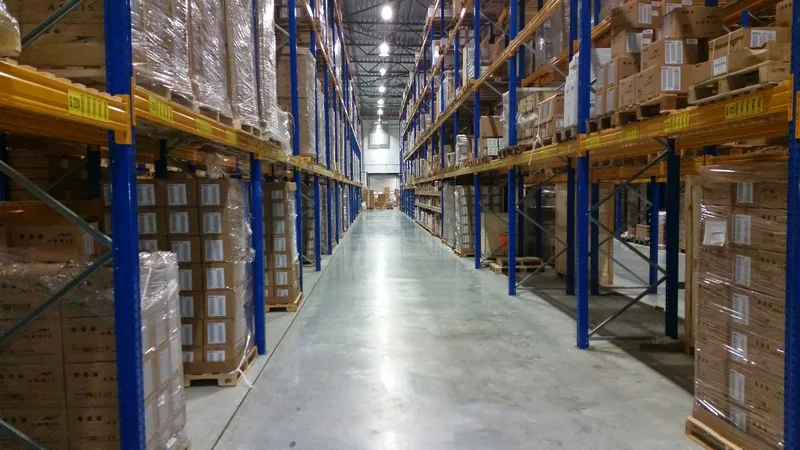 Warehouse aisle with blue and yellow racking stacked with wrapped pallets and cardboard boxes