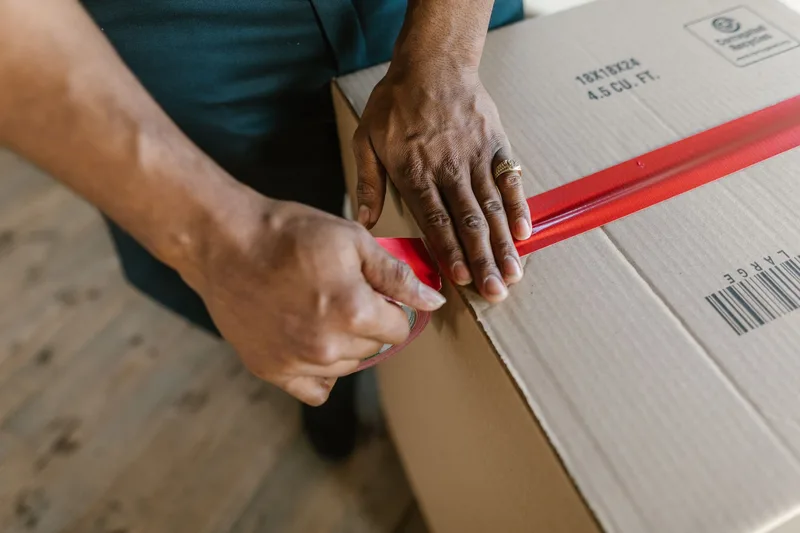 Close-up of hands sealing a cardboard shipping box with tape