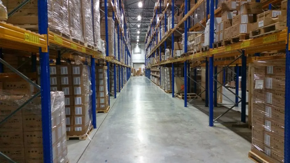 Long warehouse aisle between blue and yellow pallet racking loaded with shrink-wrapped cartons