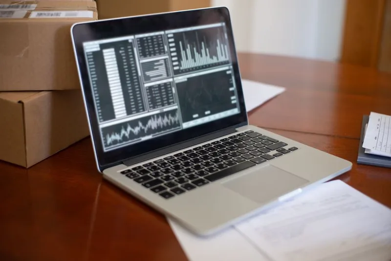 Laptop showing charts and tables on a desk beside stacked cardboard boxes