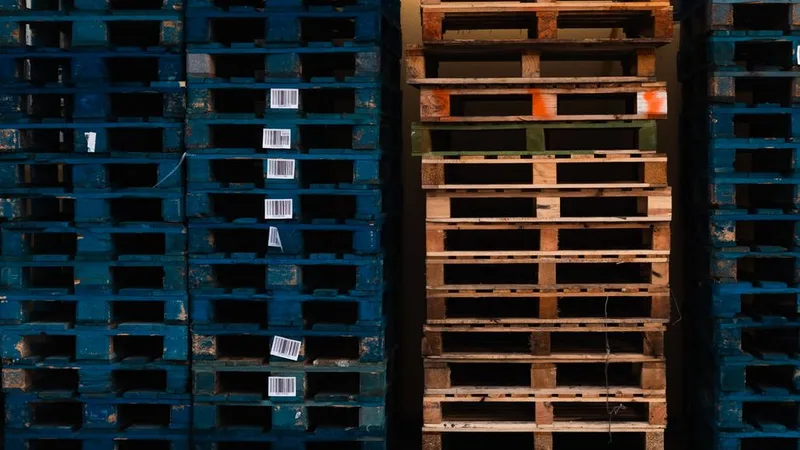 Stacks of blue and wooden pallets with small barcode labels stuck to the ends of several pallets