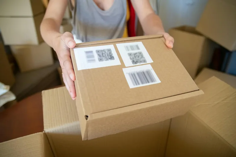 Warehouse packing station with a WMS pick list displayed on screen, showing ordered items by bin location