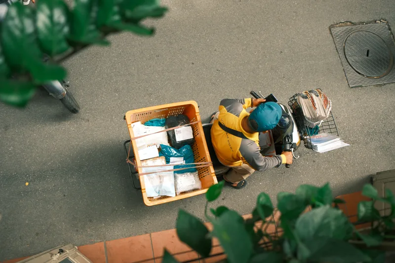 Overhead view of a courier on a scooter carrying a crate of parcels along a street